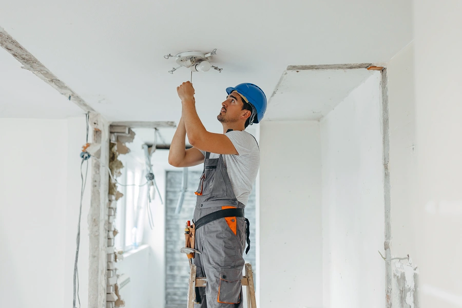 Worker fixing ceiling wiring on ladder.