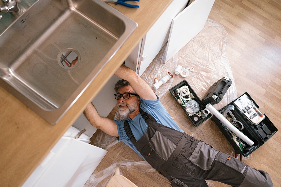 Plumber fixing kitchen sink with tools nearby.