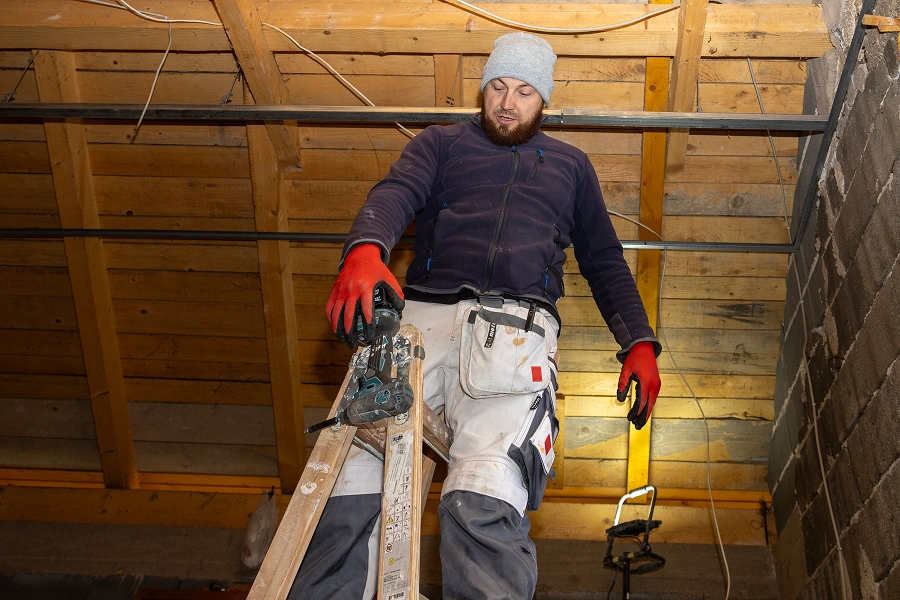 Worker on ladder in construction site attic.