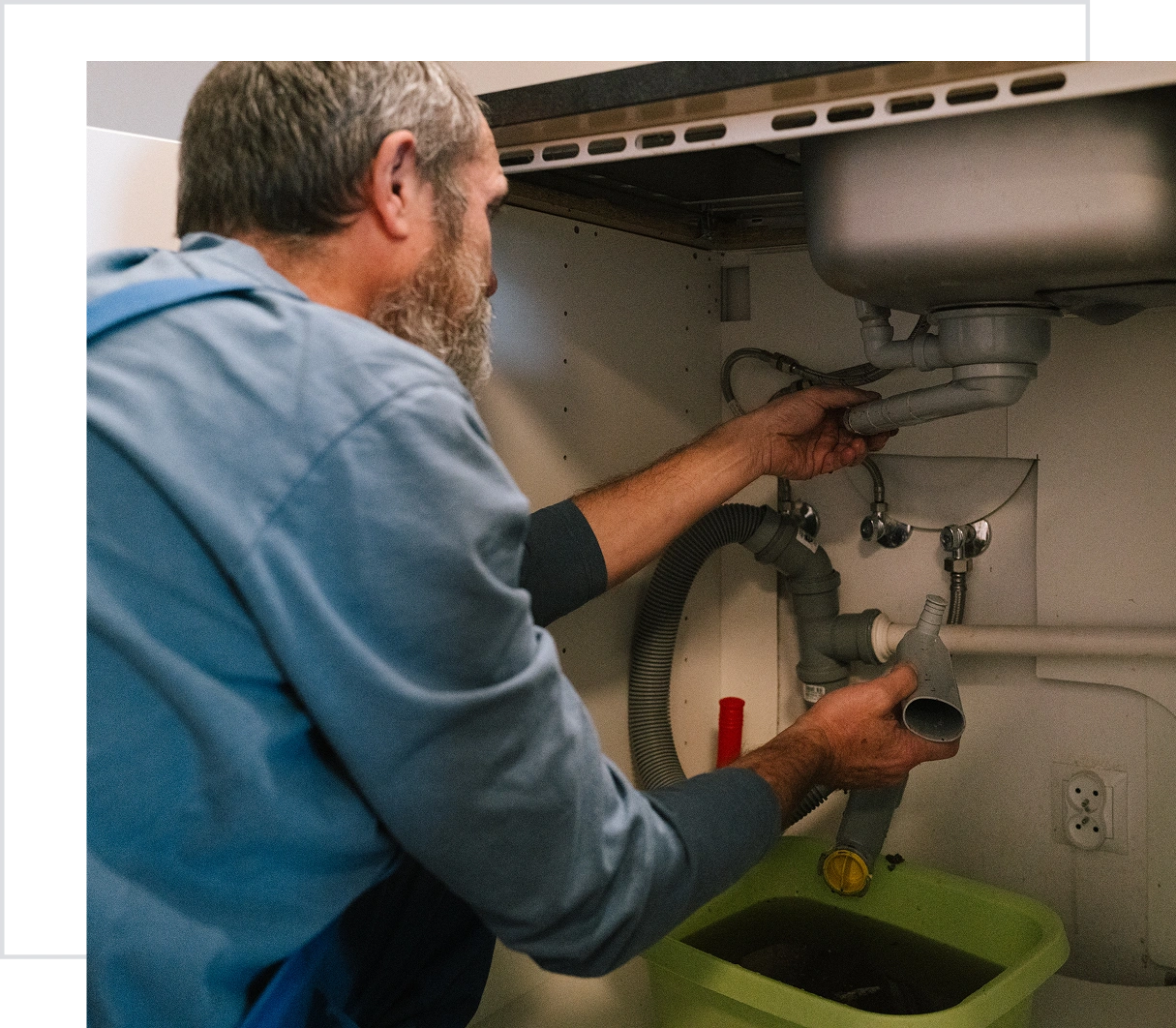 Plumber fixing sink pipes under kitchen counter.