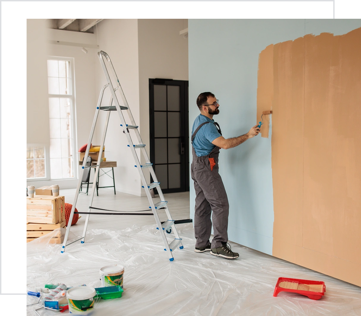Man painting wall with roller. Ladder nearby.