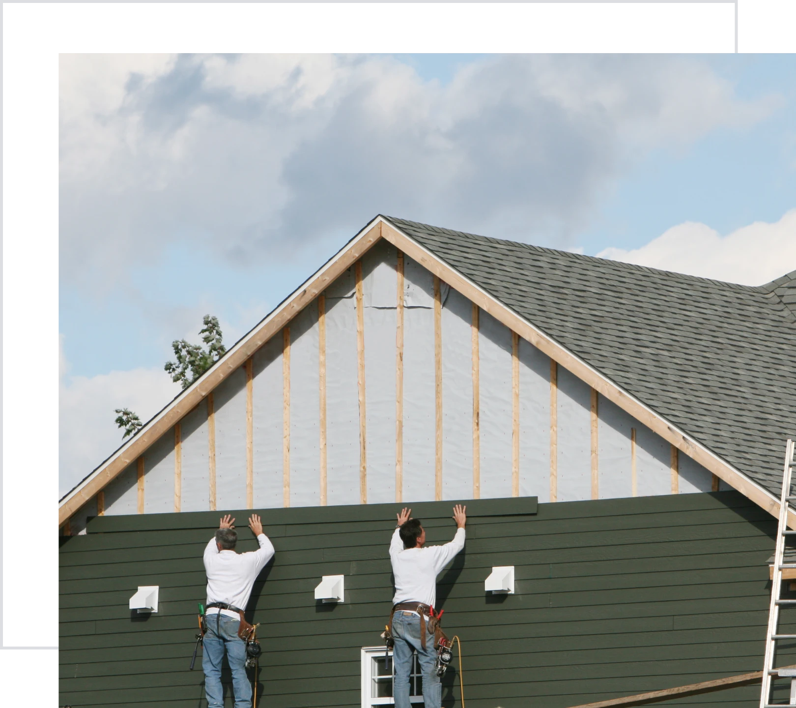 Construction workers installing siding on house.