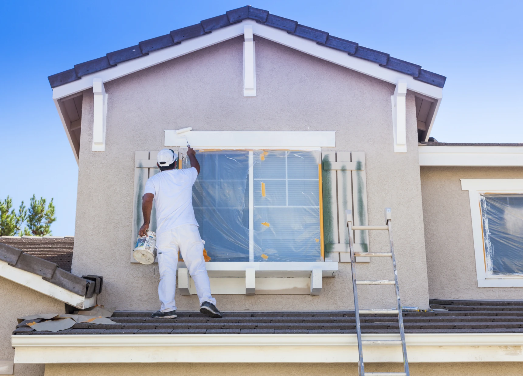 Painter working on house exterior with ladder.