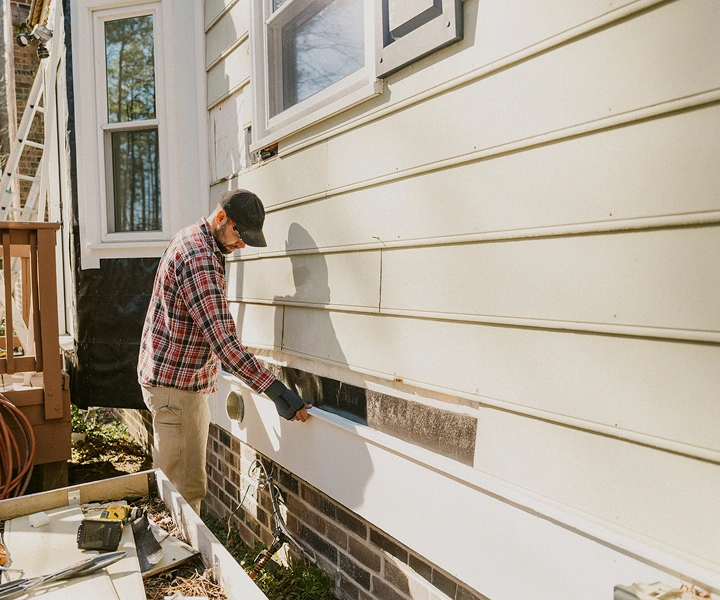 Man installing siding on house exterior wall.