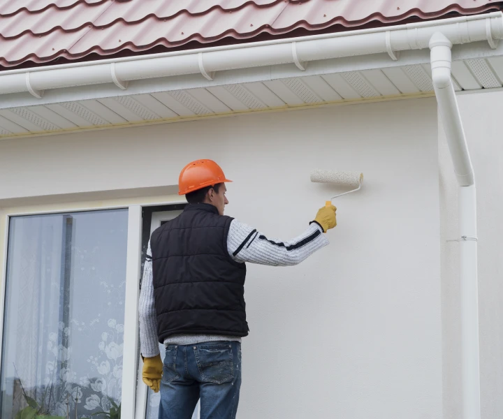Man painting house wall with roller.